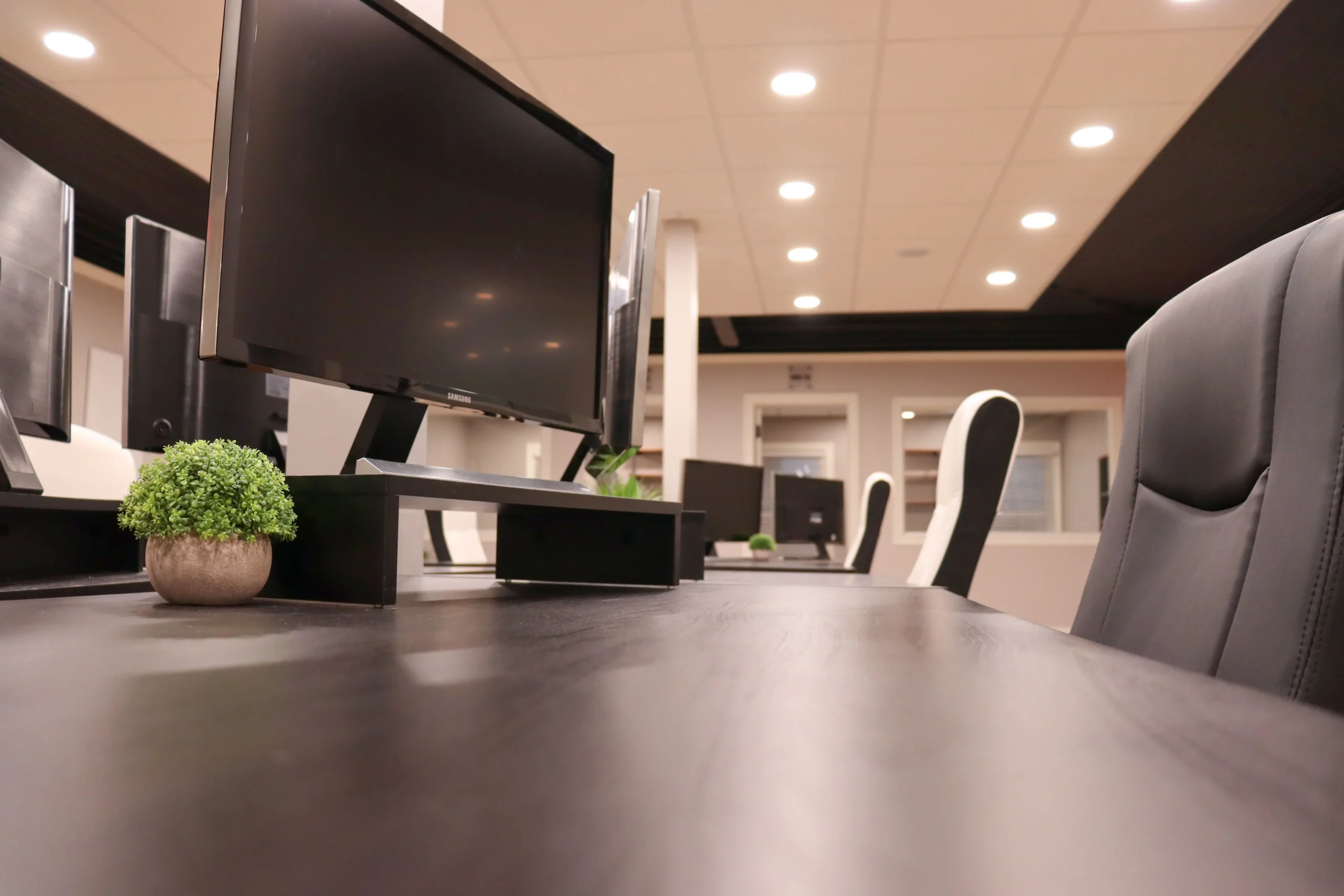 Close-up of a coworking desk setup with a monitor, plant decor, and seating at Akron Spaces